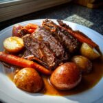 Close-up of shredded, tender pot roast served with whole carrots and small potatoes in rich brown gravy.