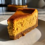 Close-up of a rich, orange slice of amazing pumpkin cheesecake with a dark graham cracker crust.