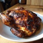 A whole roasted spatchcock chicken with deeply browned, crispy skin resting on a white plate.