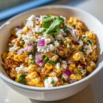 Close-up of creamy, charred corn kernels topped with crumbled white cheese, red onion, and cilantro, ready to eat as street corn salad.