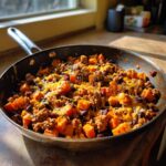 A close-up of a savory sweet potato skillet mixture with ground meat, black beans, and melted cheese.