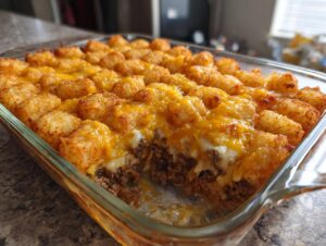 A close-up of a glass baking dish filled with amazing tater tot casserole, showing crispy tots and melted cheddar cheese over ground meat.