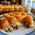A close-up serving of cheesy tater tot casserole showing crispy tots, melted cheese, and ground beef filling.