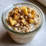 Close-up of apple cinnamon overnight oats topped with diced apples, oats, and cinnamon in a glass jar.