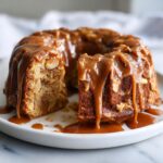 A moist apple dapple cake, shaped like a bundt, generously covered in dripping caramel sauce.
