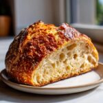A close-up of a freshly baked artisan bread loaf, sliced to show the open, airy crumb and dark, blistered crust.