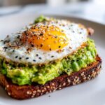 Close-up of creamy avocado toast topped with a sunny-side-up egg and everything bagel seasoning.