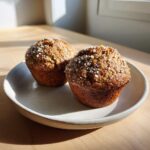 Two freshly baked banana oatmeal muffins topped with coarse sugar crystals, resting on a light ceramic plate.