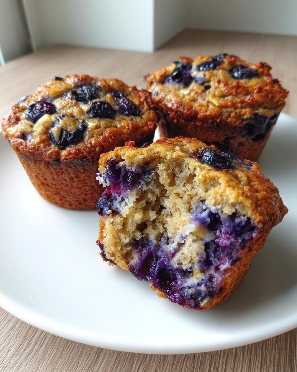 Close-up of three blueberry protein muffins, one broken open showing the moist interior and rich blueberry filling.
