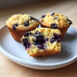 Close-up of three blueberry protein muffins, one cut in half showing the moist interior.