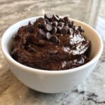 A white bowl filled with thick, rich brownie batter dip, topped generously with semi-sweet chocolate chips.