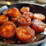 Thick-cut, round candied sweet potatoes glistening with a rich brown sugar glaze in a dark skillet.