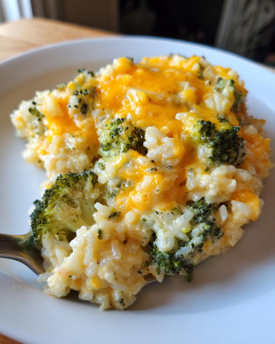 A spoonful of creamy, cheesy broccoli rice casserole topped with melted cheddar cheese.
