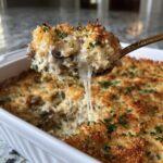 A spoonful of hot, cheesy stuffed mushroom dip showing long cheese pulls over the baking dish.