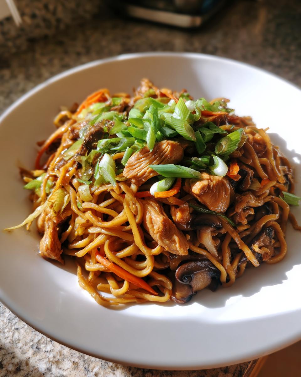 A close-up of a bowl filled with homemade chicken chow mein recipe, topped generously with sliced green onions.