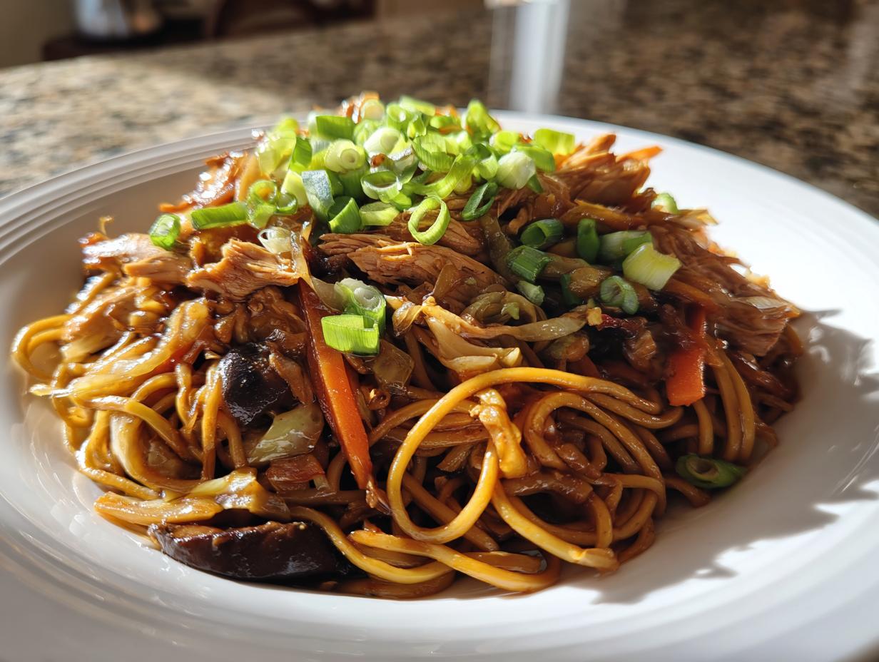 A close-up of a serving of flavorful chicken chow mein recipe, topped with fresh green onions.
