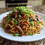 A plate of savory chicken chow mein recipe noodles mixed with mushrooms, carrots, and topped generously with fresh green onions.