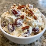 A white bowl filled with creamy Chicken Salad Chick Grape Salad, topped with red grapes, pecans, and a sprinkle of cinnamon.