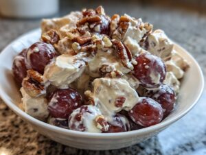 A close-up of creamy Chicken Salad Chick Grape Salad featuring red grapes, chicken chunks, and chopped pecans.