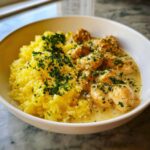 Close-up of chicken scampi in creamy sauce next to yellow garlic parmesan rice, garnished with parsley.