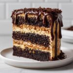 A tall slice of decadent chocolate peanut butter cake with multiple layers and chocolate ganache drip.