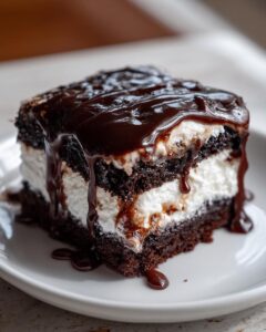 Close-up of a moist slice of chocolate poke cake layered with white filling and drizzled heavily with dark chocolate fudge.