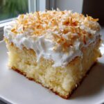 A moist slice of coconut poke cake topped with white frosting and toasted coconut flakes.