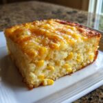 A square slice of moist cream cheese corn casserole, studded with whole corn kernels and topped with melted golden cheese.
