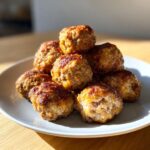 A stack of golden brown, freshly baked cream cheese sausage balls piled on a light gray plate.