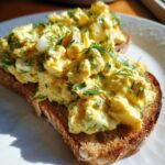 Close-up of creamy egg salad generously piled on a slice of toasted bread, garnished with fresh dill.