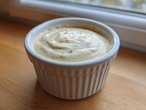 A close-up of thick, creamy garlic sauce seasoned with pepper, served in a white fluted ramekin.
