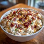 Close-up of a creamy Million Dollar Dip topped generously with crumbled bacon and chives.