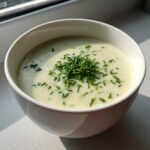 A close-up of a creamy bowl of potato leek soup garnished generously with freshly chopped chives.