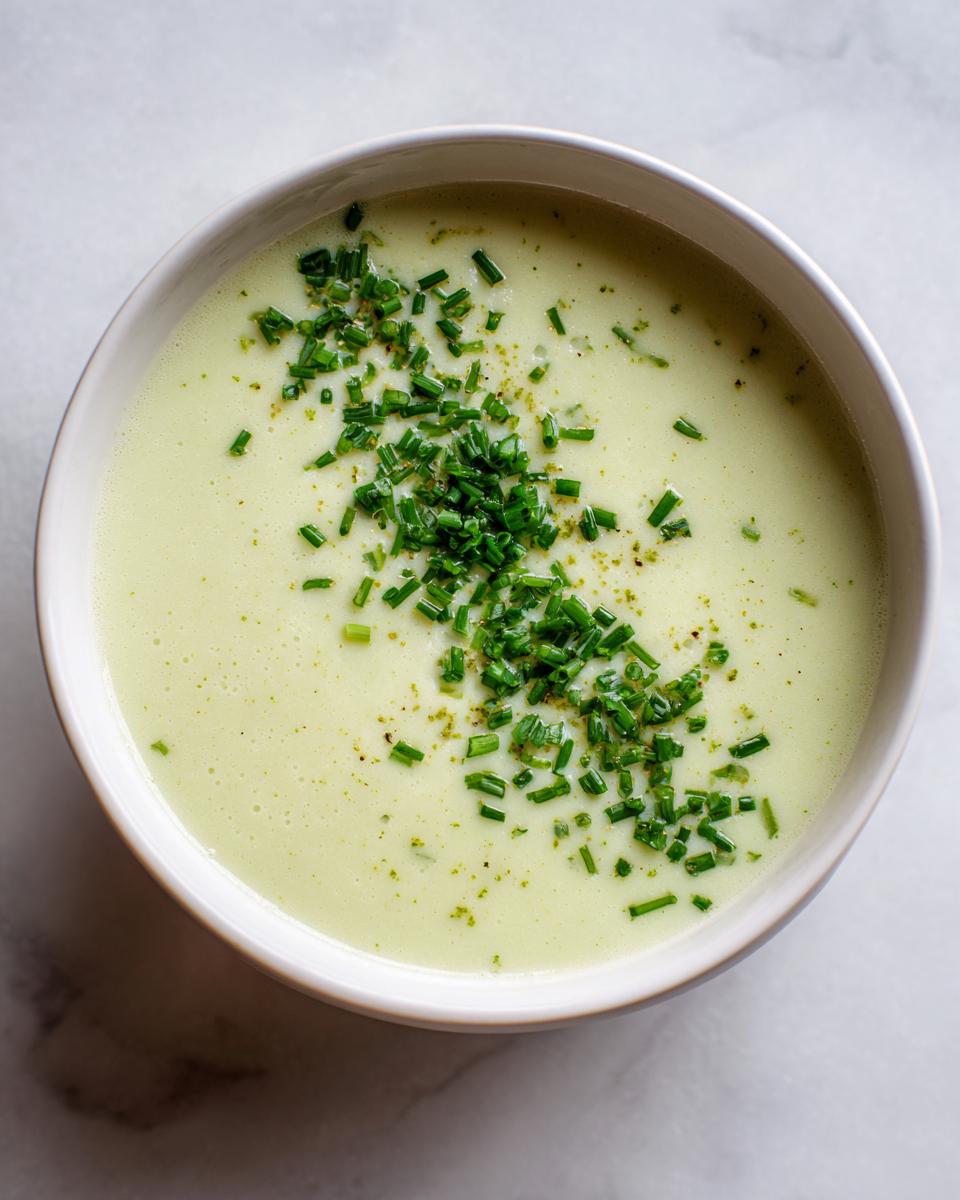 Overhead view of a bowl of creamy potato leek soup garnished generously with chopped fresh chives.
