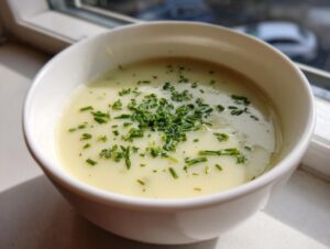 A close-up of creamy potato leek soup in a white bowl, topped generously with fresh chopped chives.