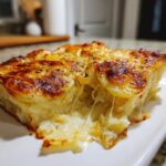A close-up of a serving of creamy scalloped potatoes showing a dramatic cheese pull and golden brown top.