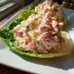 Close-up of creamy seafood salad served in a crisp lettuce cup on a white plate.