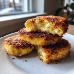 A stack of three golden-brown, crispy mashed potato cakes, with the top one broken open showing the fluffy interior.