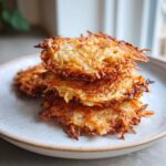 A close-up stack of four golden-brown, crispy potato latkes served on a speckled white plate.