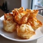 A close-up of several golden brown, crispy rice paper dumplings piled high on a white plate.