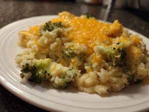 A close-up of a creamy serving of broccoli rice topped with melted cheddar cheese on a white plate.