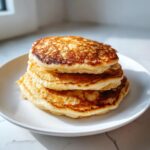 A stack of three fluffy, golden-brown almond flour pancakes served on a white plate.
