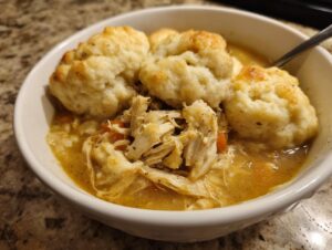 A close-up of a bowl of rich chicken and dumplings, featuring shredded chicken and fluffy, golden-brown dumplings.
