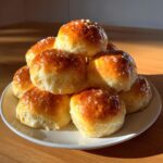 A stack of golden-brown, fluffy dinner rolls topped with a shiny glaze and coarse salt crystals.