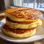 A stack of three fluffy, golden-brown greek yogurt pancakes on a white plate.