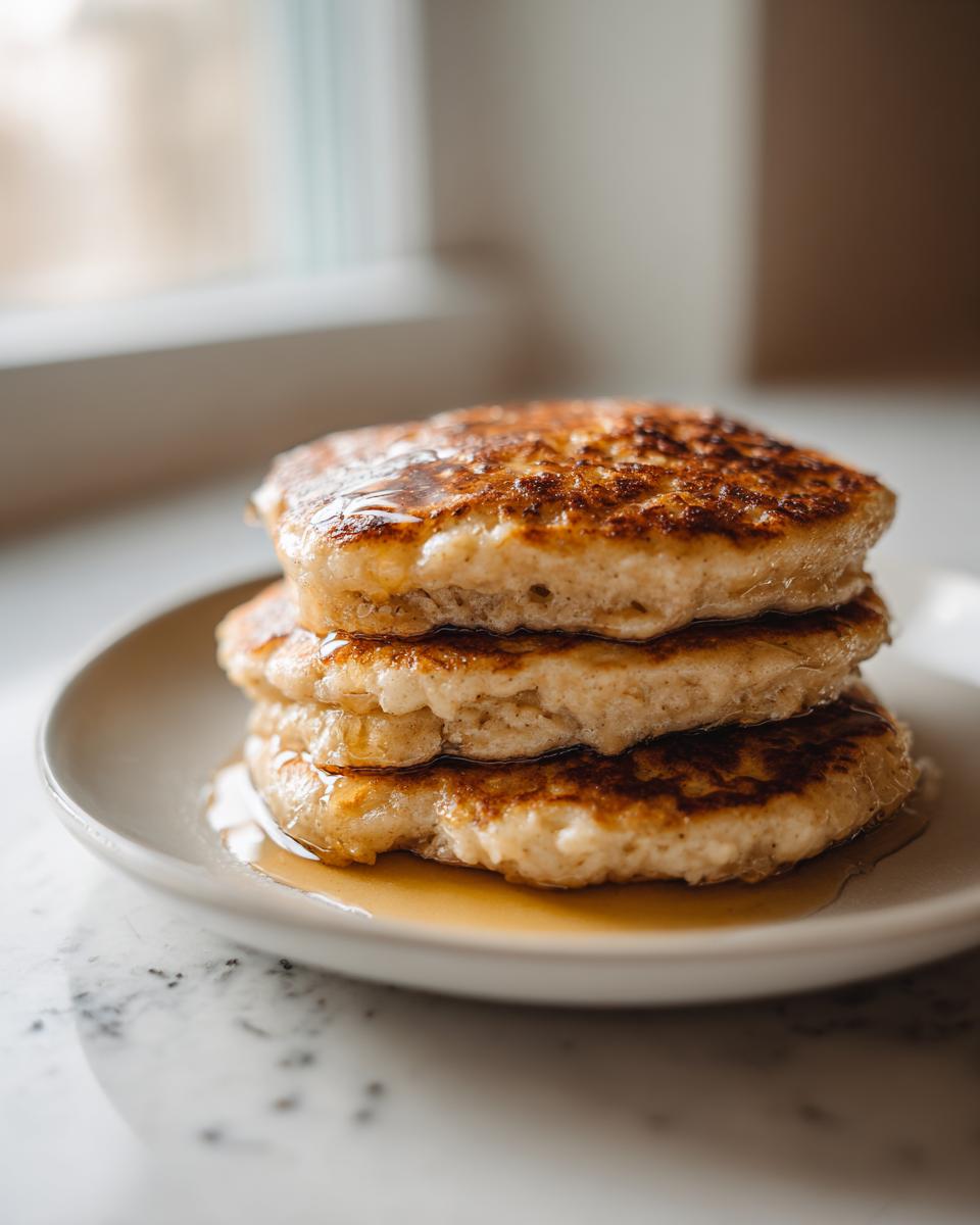 Close-up of a stack of three fluffy oatmeal pancakes drizzled generously with golden syrup.