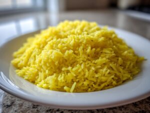 Close-up of bright yellow, fluffy turmeric rice served on a white plate, ready to eat.