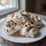 A plate of fluffy, white forgotten cookies topped generously with chocolate chips and chopped pecans.