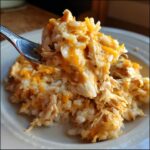 A fork lifting a generous bite of creamy crock pot chicken and rice mixed with melted cheddar cheese.