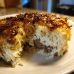 A cross-section of savory french onion butter rice molded into a cake shape, showing white rice, a dark meat filling, and caramelized onions on top.